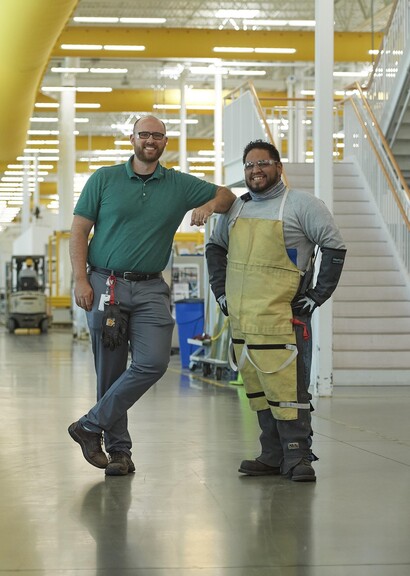 Deux collègues souriant dans un bâtiment de fabrication.