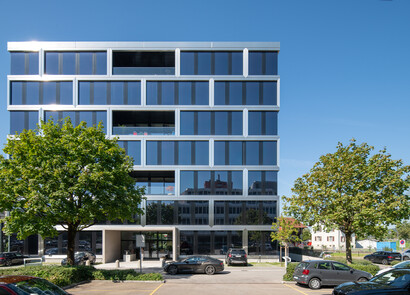 Façade du bâtiment Alpha équipée de SageGlass Bright Silver. Quelques arbres et voitures devant le bâtiment.