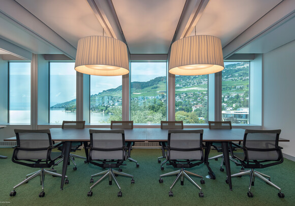 Intérieur de la salle de réunion avec des vitres intelligentes donnant sur l'eau et les montagnes. 