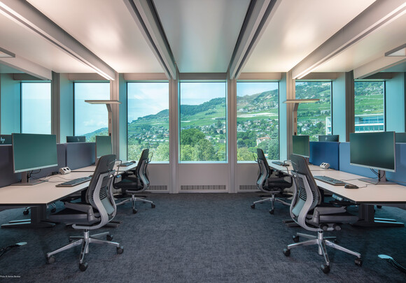 Espace de travail collaboratif avec du vitrage intelligent de gauche à droite donnant sur un flanc de montagne.