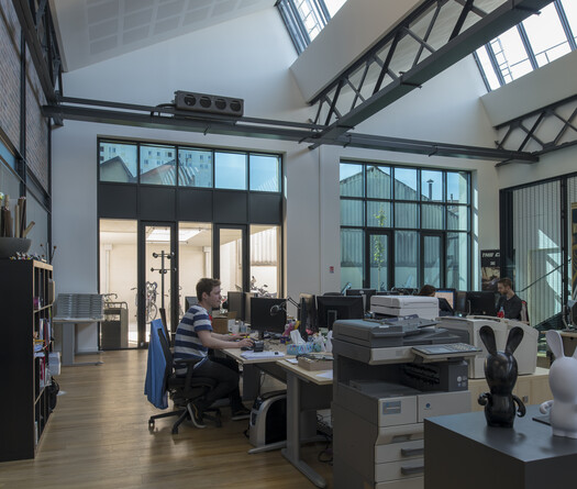 Vue de l'intérieur du bâtiment. Des personnes travaillent sur des ordinateurs, certains vitrages sont teintés, d'autres non.