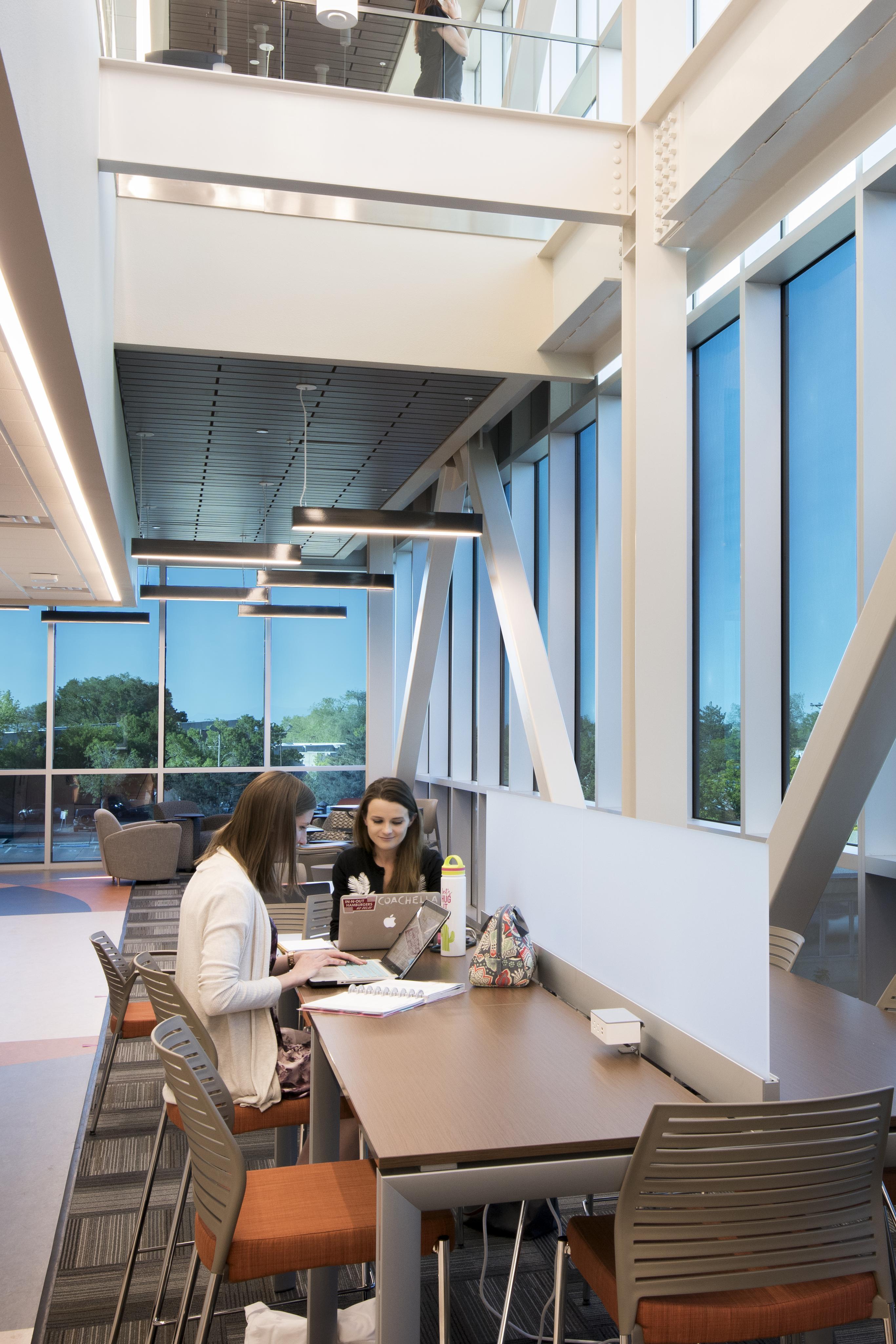 Deux collègues collaborent à une table dans l'espace commun d'un immeuble de bureaux avec du vitrage intelligent.