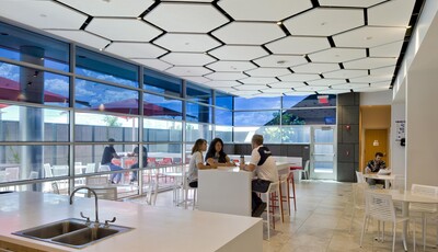 Intérieur d'un bâtiment moderne en verre avec de grandes fenêtres et un groupe de personnes déjeunant à des tables.