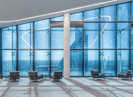 Espace commun intérieur d'un immeuble de bureaux avec, de gauche à droite, des chaises longues et des baies vitrées intelligentes. 