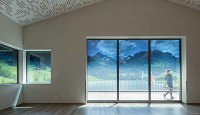 Espace intérieur d'une maison avec des vitres intelligentes donnant sur les montagnes avec une femme marchant sur la terrasse. 