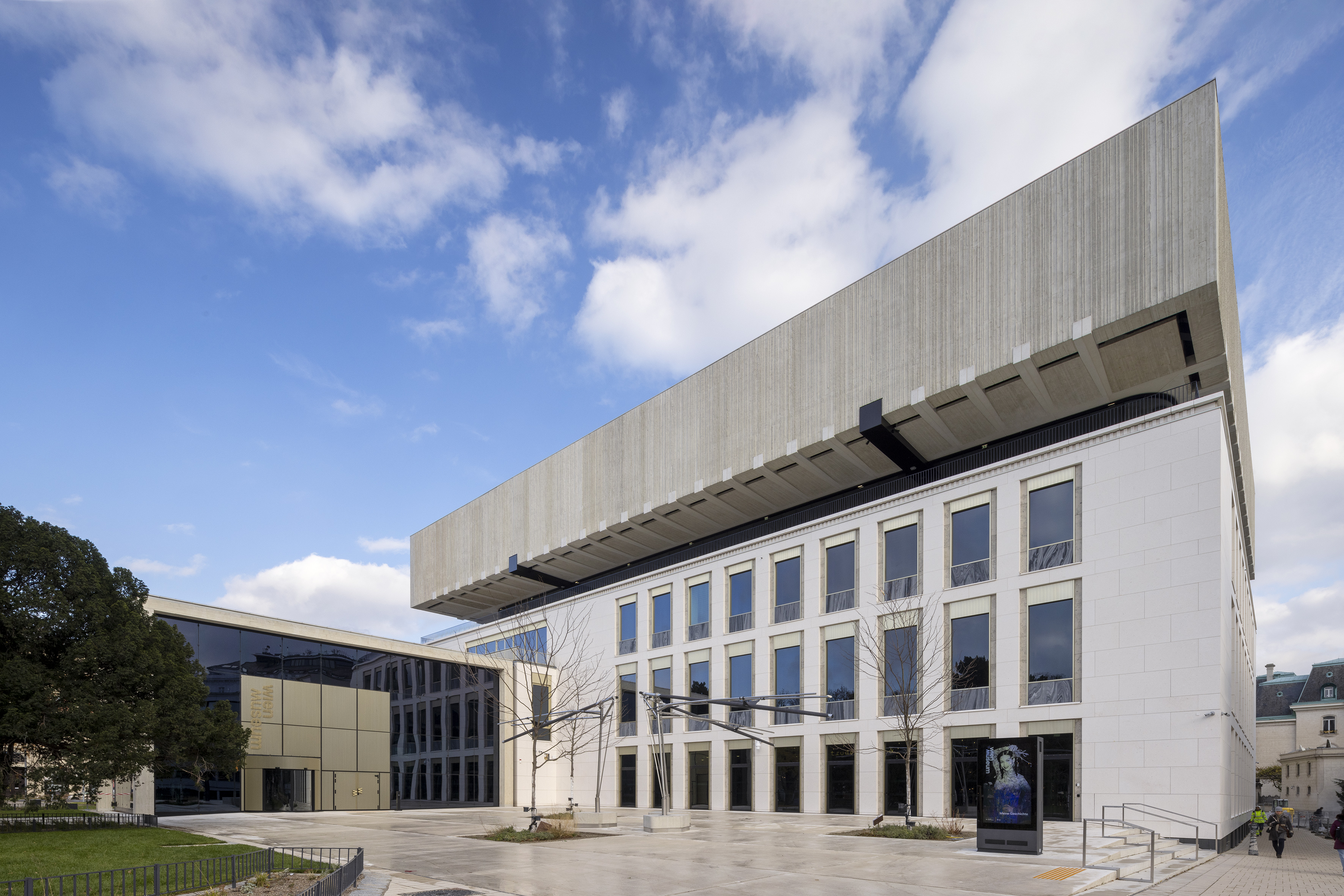 View from the outside of the building. The building is white and grey. The left side is completely glazed.