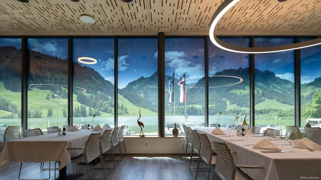 Vue intérieure d'un restaurant ou d'une salle de banquet avec des fenêtres allant du sol au plafond et offrant une vue imprenable sur la nature.